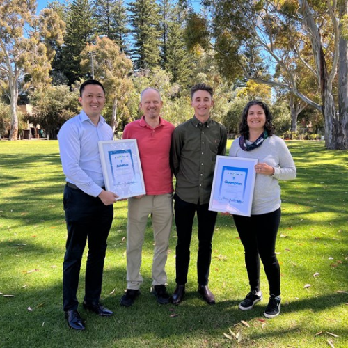  =Four people standing together in parkland, two of the people are holding award certificates - opens in a new tab